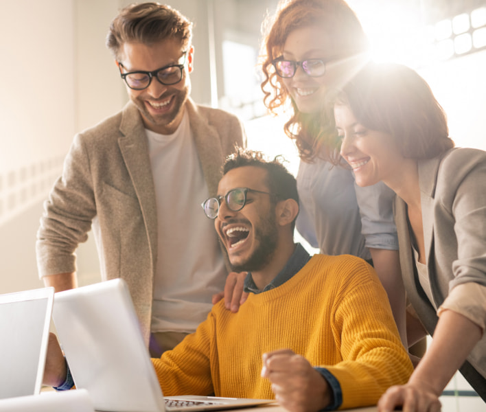 Fotografia de um grupo de pessoas sorrindo e olhando para um notebook